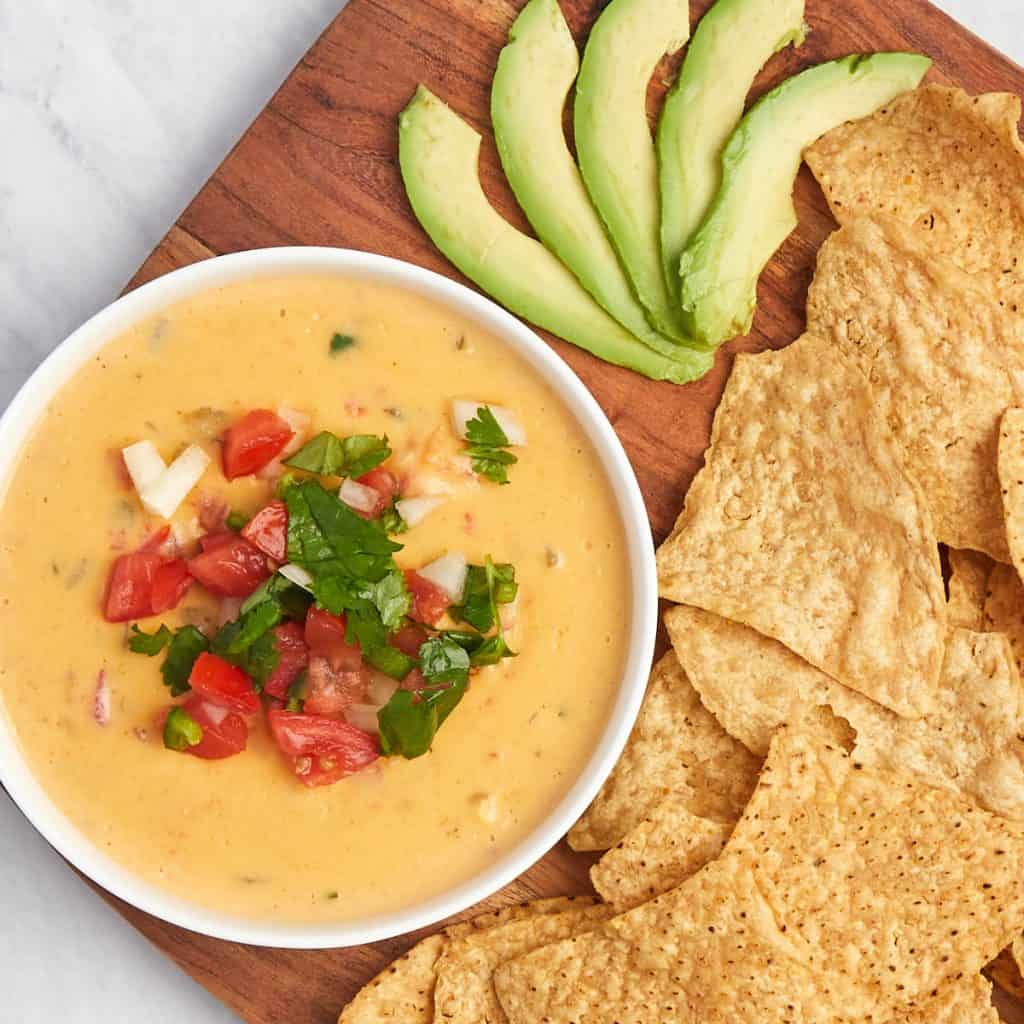tex-mex queso in serving bowl topped with pico de gallo with chips and avocado.