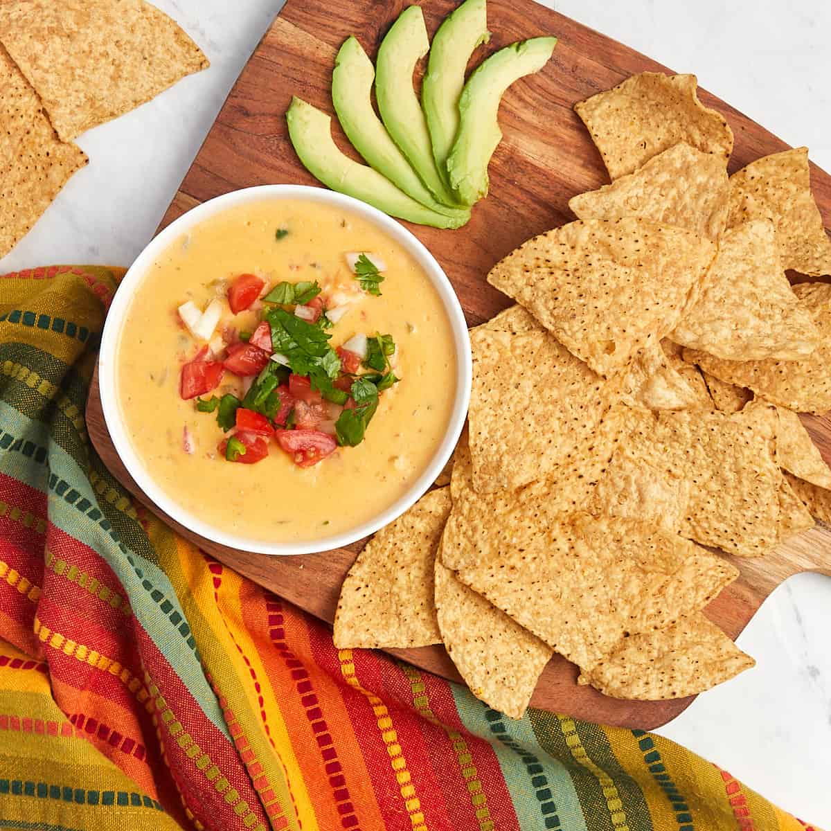 tex-mex queso in serving bowl topped with pico de gallo with chips and avocado