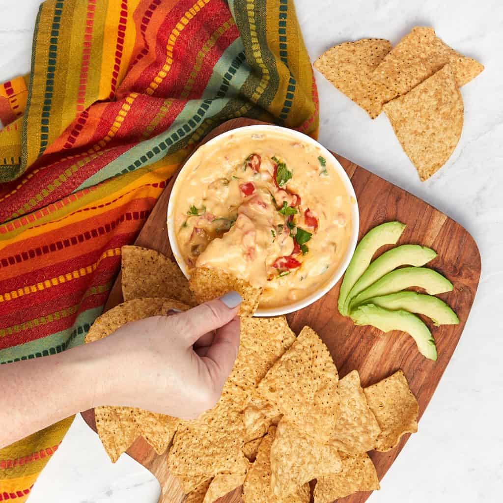 tex-mex queso in serving bowl topped with pico de gallo with chips and avocado.