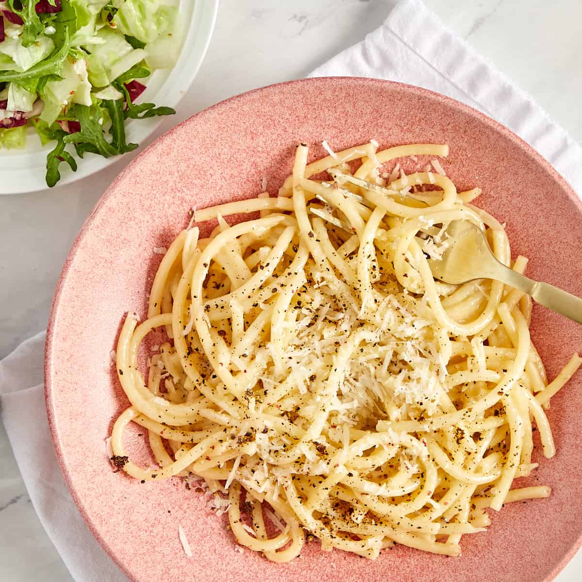 bucatini cacio e pepe in a bowl with a salad on the side.