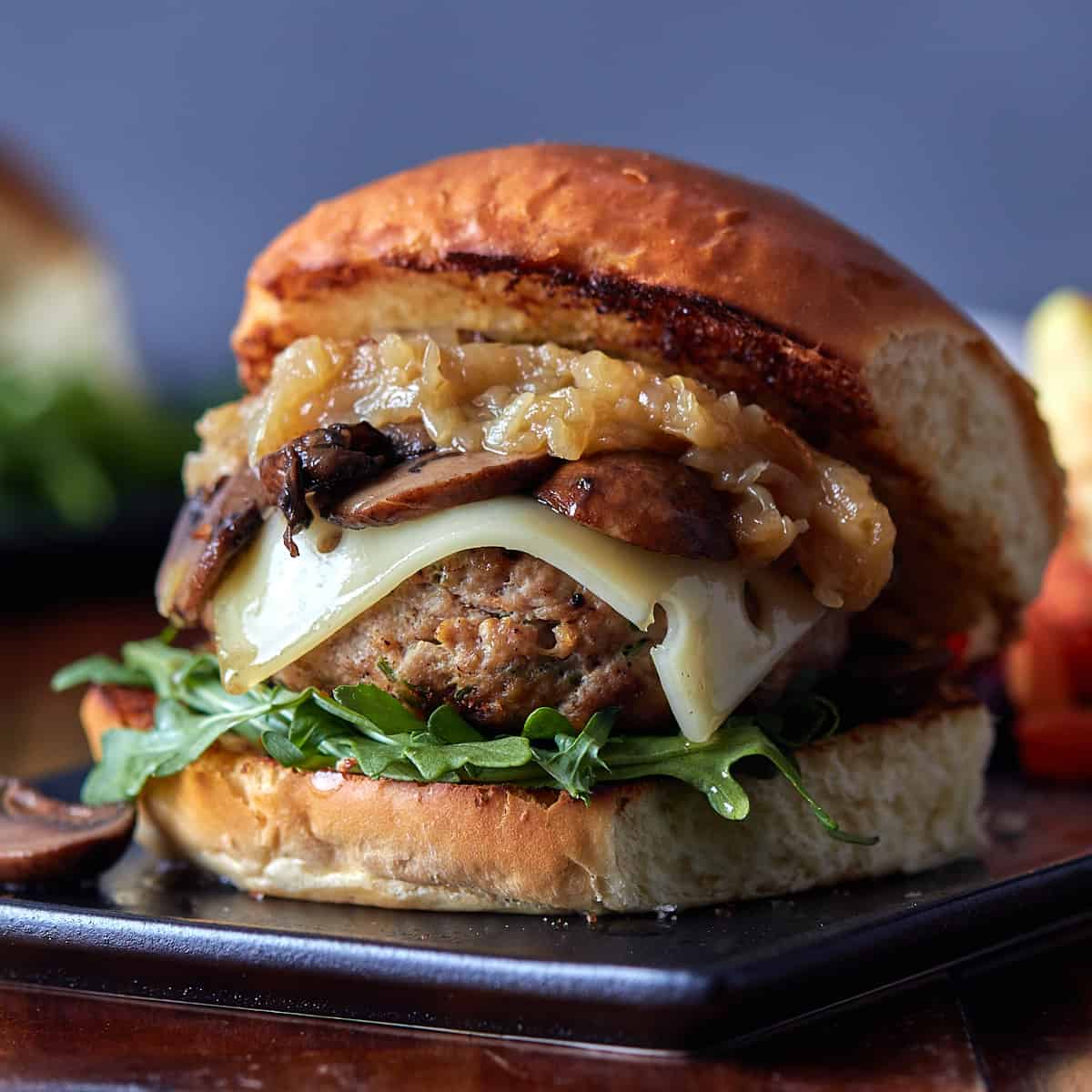 burger on plate topped with caramelized onions, mushrooms, and swiss cheese