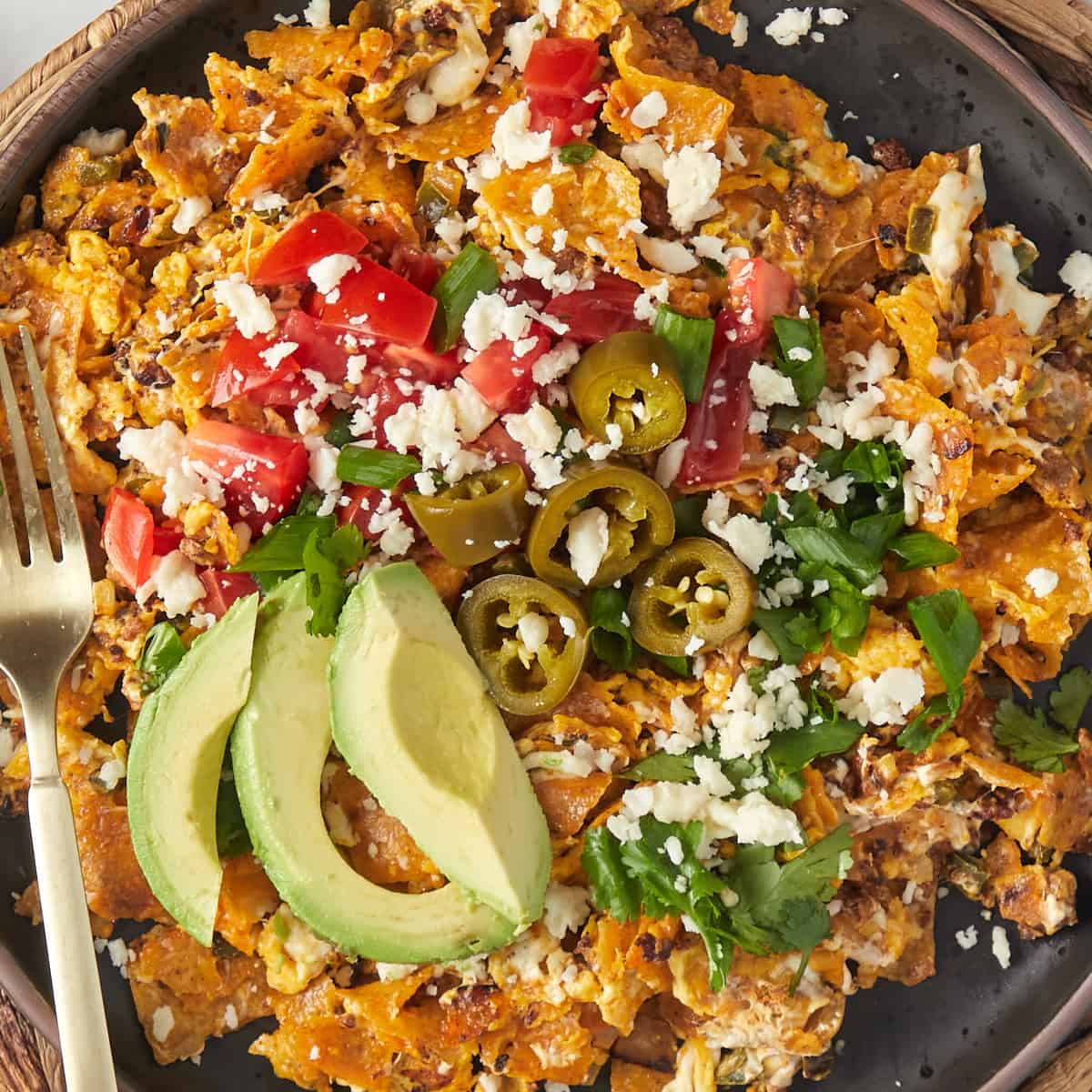 tex-mex migas on a plate topped with tomatoes, avocado, jalapeños, and cheese