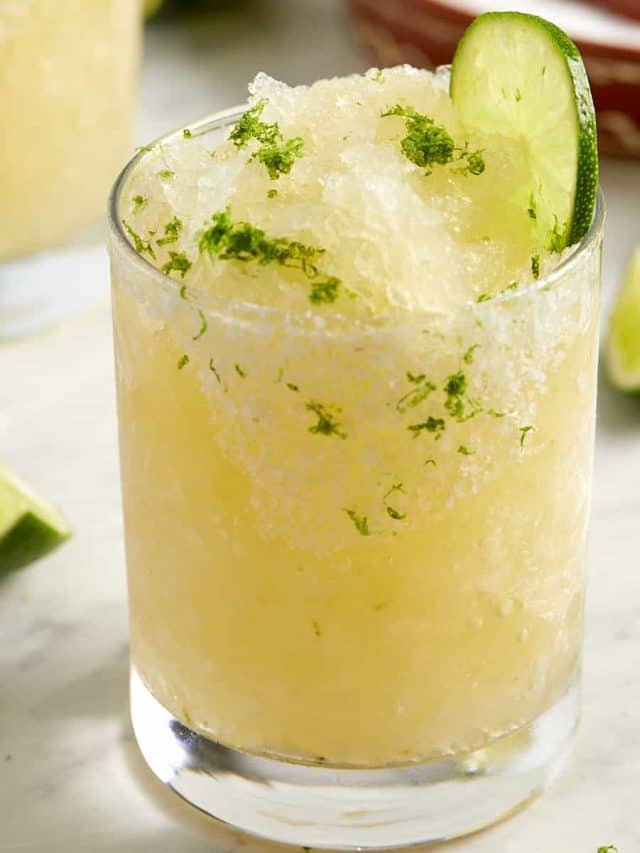 freezer margaritas in a glass with a lime garnish and a sprinkle of lime zest on top
