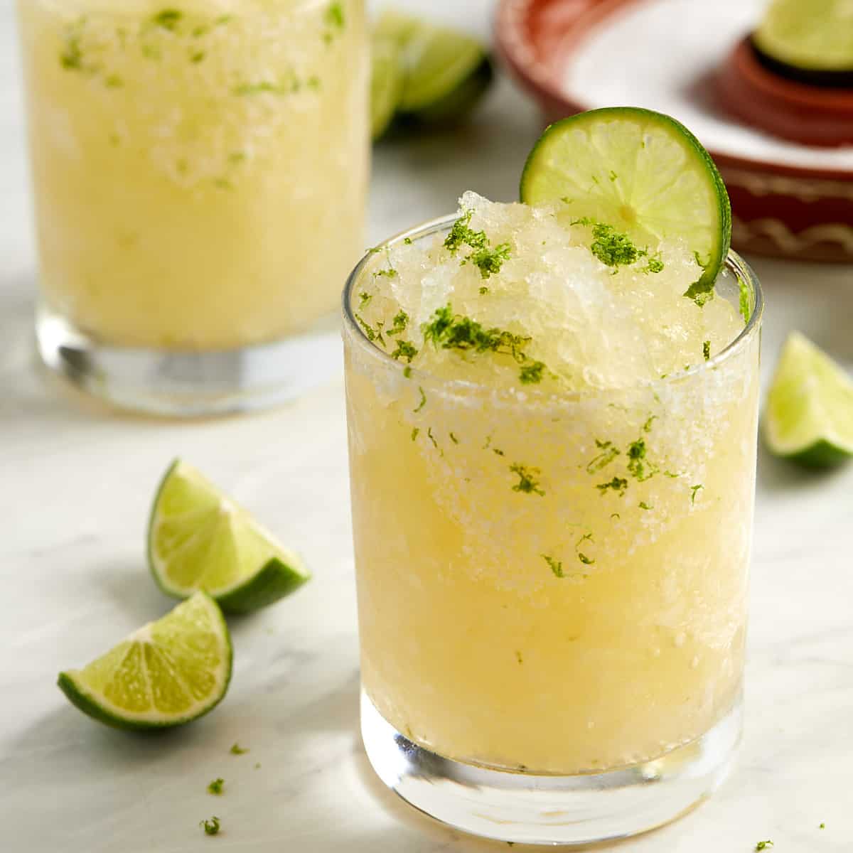 freezer margaritas in a glass with a lime garnish and a sprinkle of lime zest on top