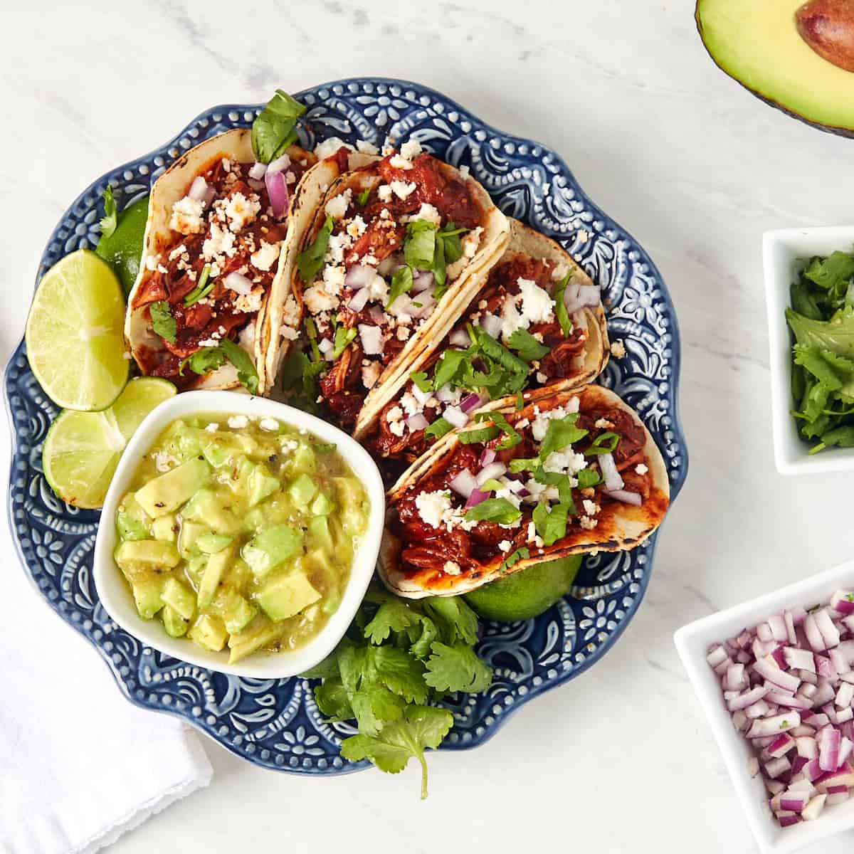 red chile chicken street tacos on a plate with avocado on the side