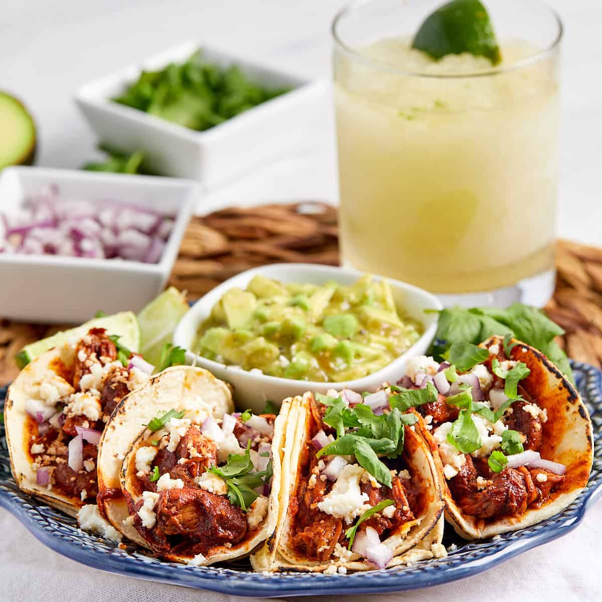 red chile chicken street tacos on a plate with avocado on the side and a margarita