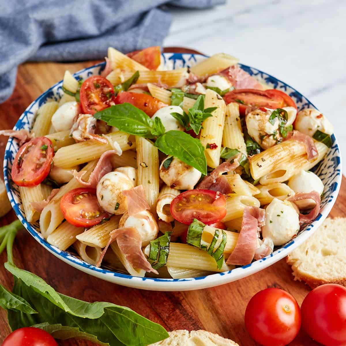 caprese pasta salad in a bowl with sliced bread and tomatoes on the side