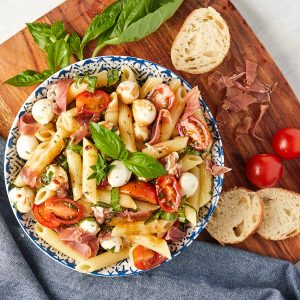 caprese pasta salad in a bowl with sliced bread and tomatoes on the side