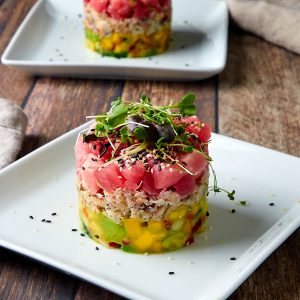 crab and ahi tuna tower on a white plate with a sprinkle of black and white sesame seeds and topped with microgreens