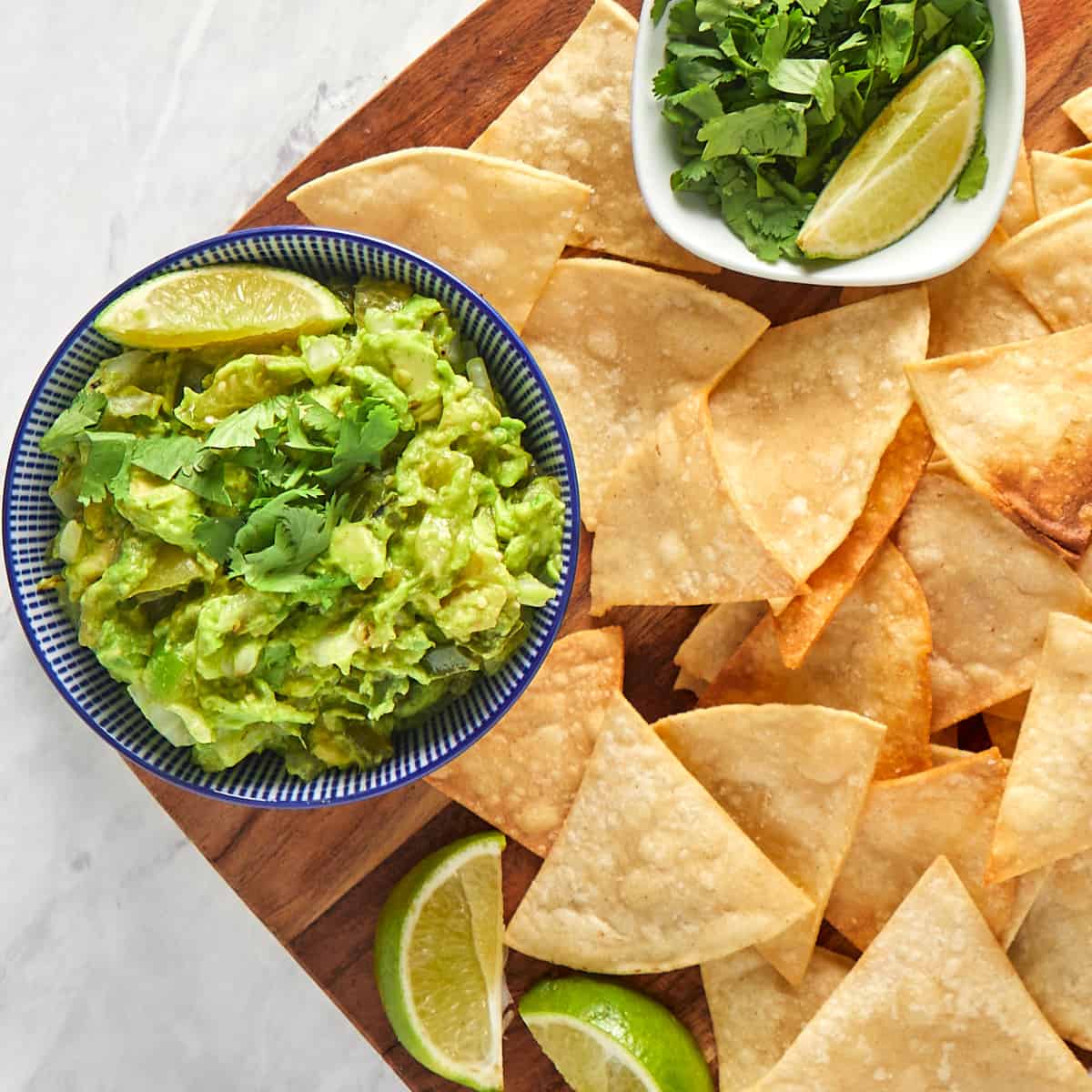 guacamole in a bowl with two lime wedges surrounded by chips