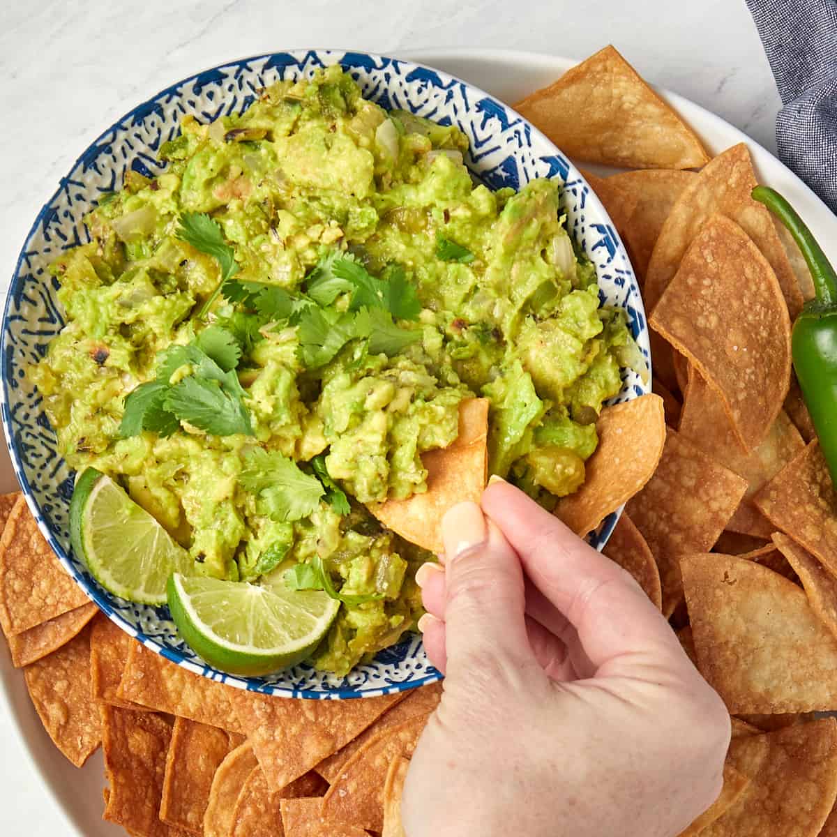 guacamole in a bowl surrounded by chips with someone dipping a chip in the bowl