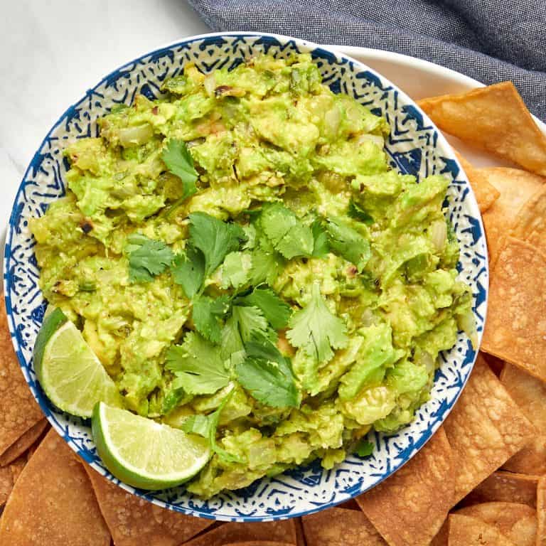 guacamole in a bowl with two lime wedges surrounded by chips