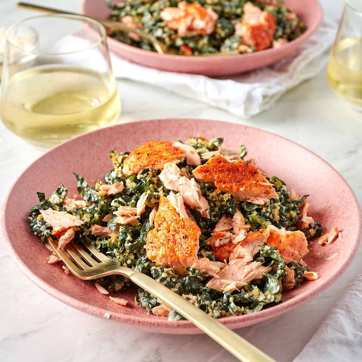 kale caesar salad in a pink bowl with a fork topped with baked salmon