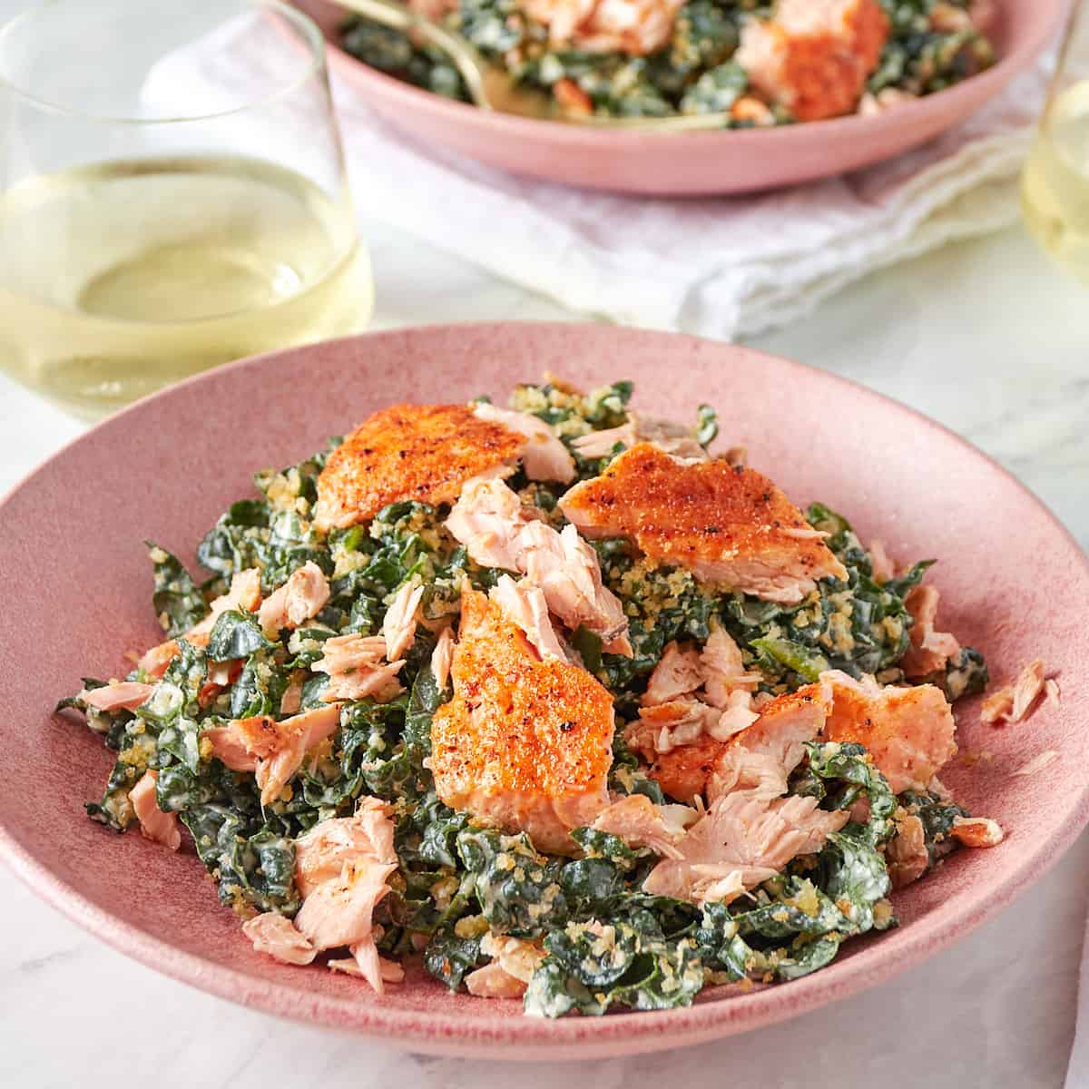 kale caesar salad with salmon in a pink bowl with a glass of wine