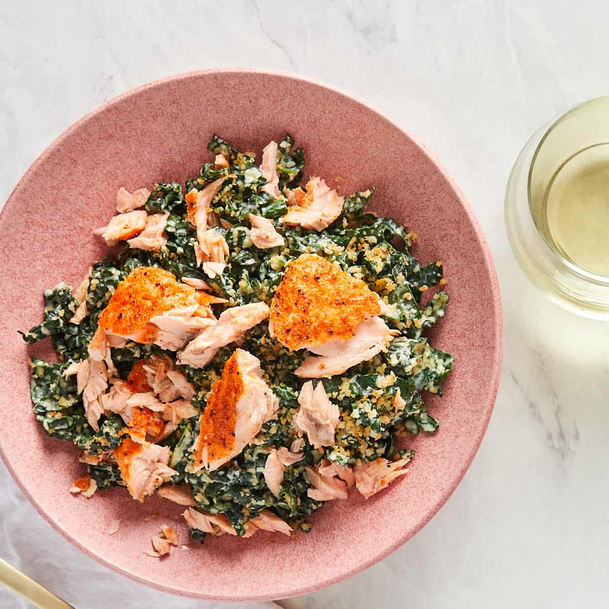 kale caesar salad with salmon in a pink bowl with a glass of wine