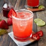 strawberry margarita on the rocks in a glass rimmed with sugar and garnished with a strawberry