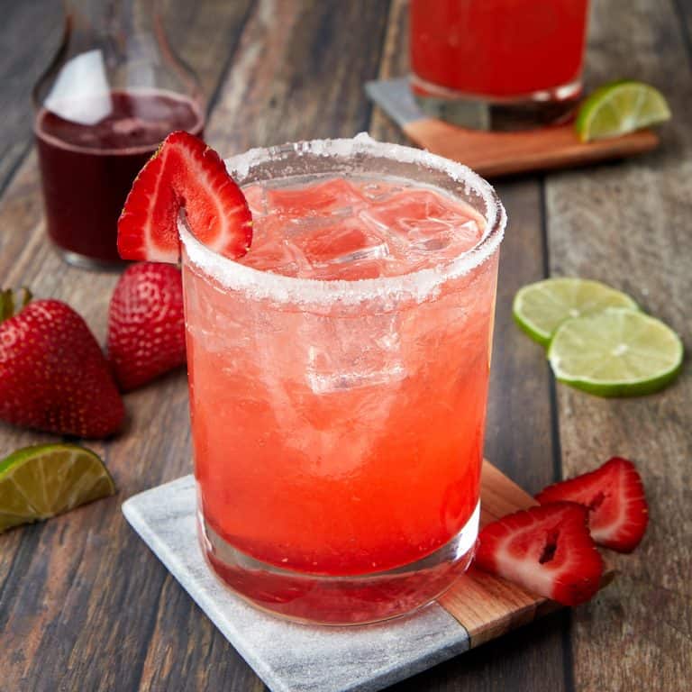 strawberry margarita on the rocks in a glass rimmed with sugar and garnished with a strawberry
