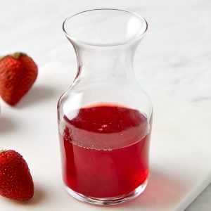 strawberry simple syrup in a glass container with strawberries placed around container for decoration