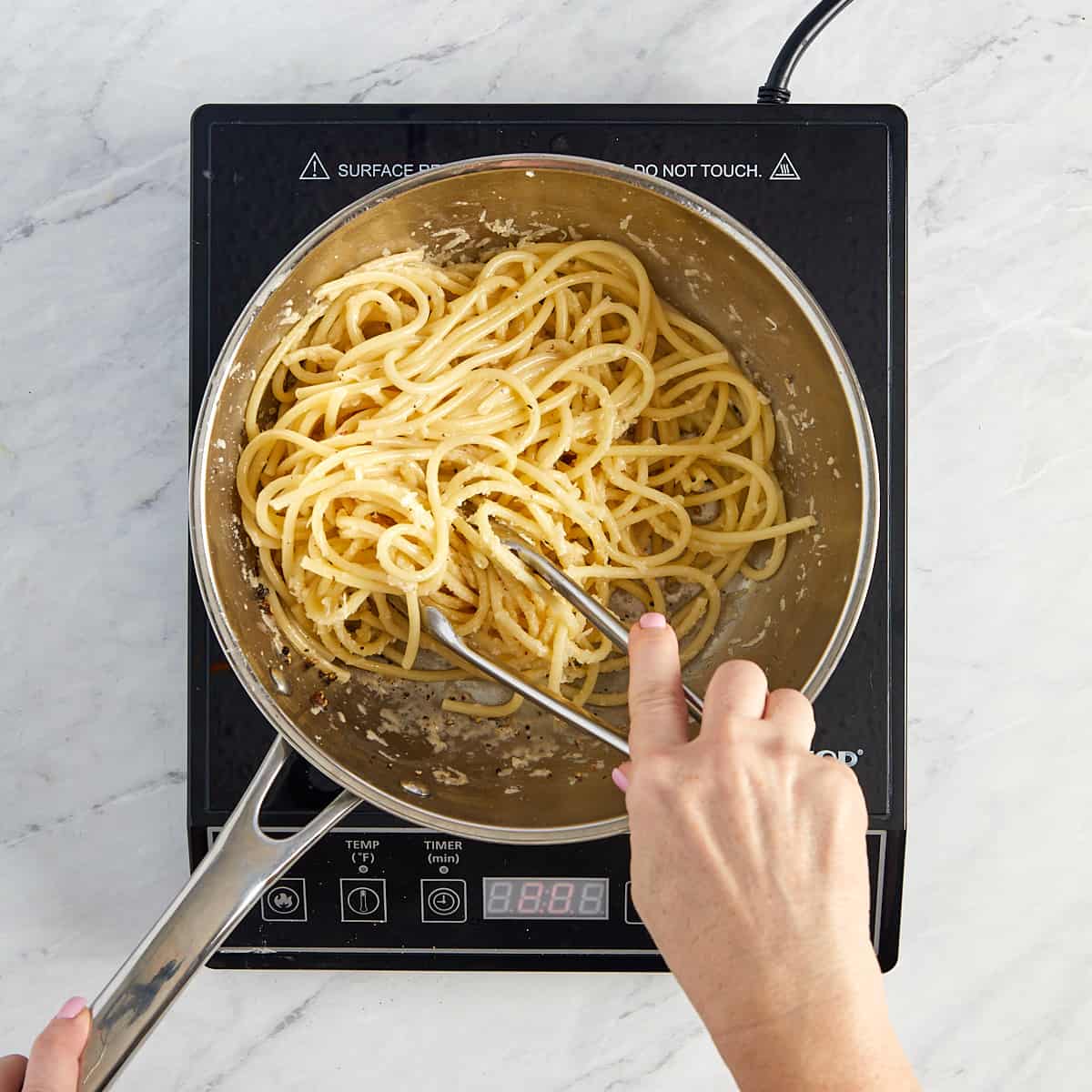 pasta being tossed with cheese to form sauce.
