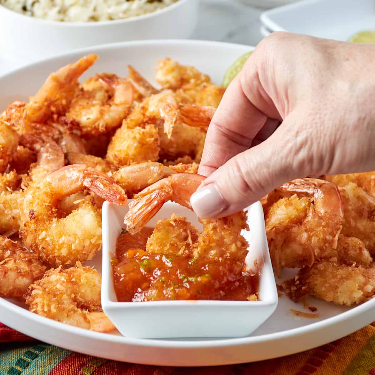 coconut shrimp on a white plate with one being dipped into a side of orange dipping sauce