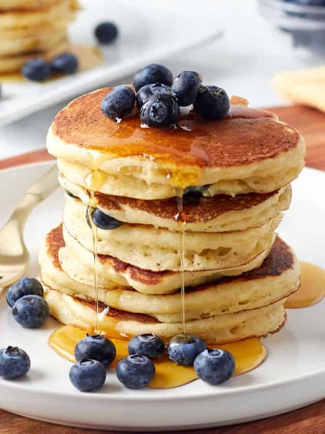stack of buttermilk pancakes on a plate with blueberries and syrup