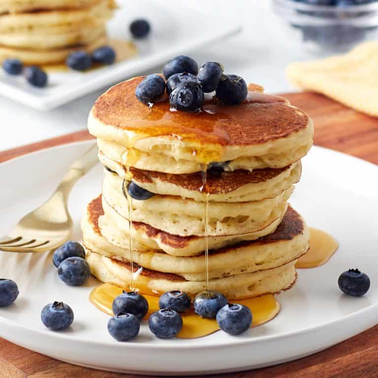 stack of buttermilk pancakes on a plate with blueberries and syrup