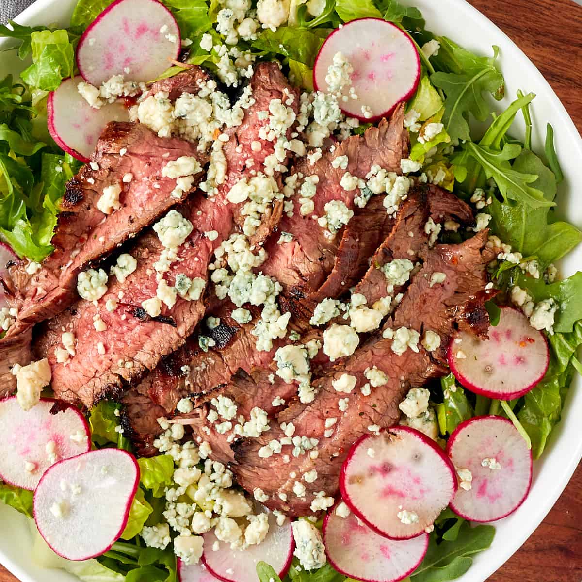 grilled marinated flank steak on top of a salad