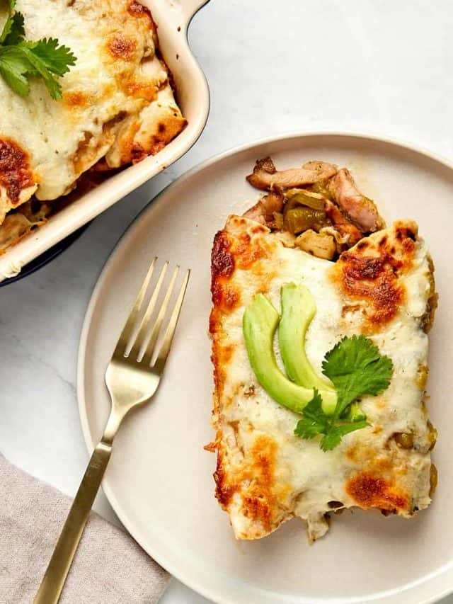 two cooked enchiladas on a plate topped with avocado slices