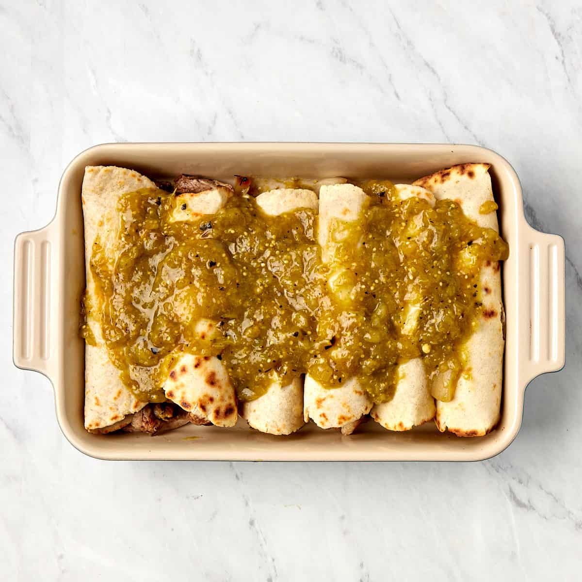 uncooked enchiladas in a casserole dish topped with tomatillo sauce
