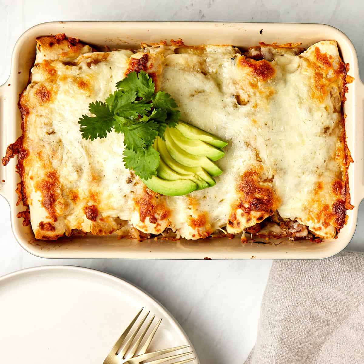 cooked enchiladas in a cassarole dish topped with cilantro and slices of avocado