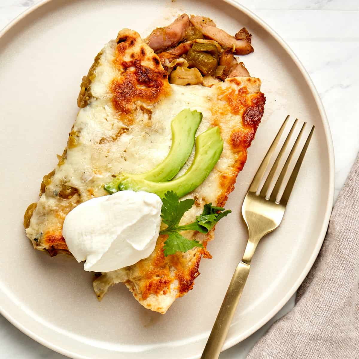 two cooked enchiladas on a plate topped with avocado slices and sour cream