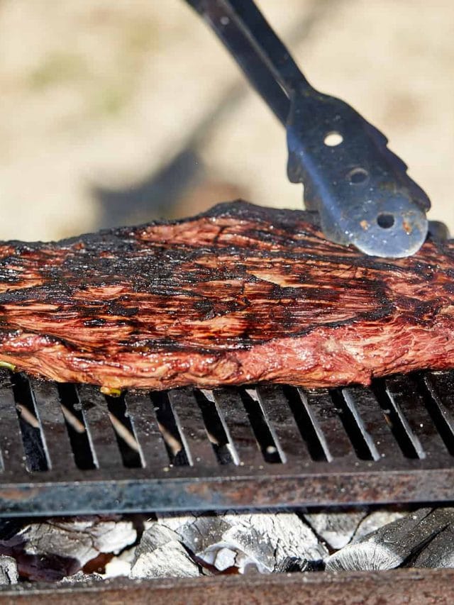 marinated flank steak being cooked on a charcoal grill