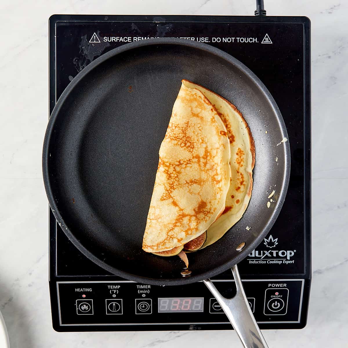 crepe being folded in half in a pan on a cooktop