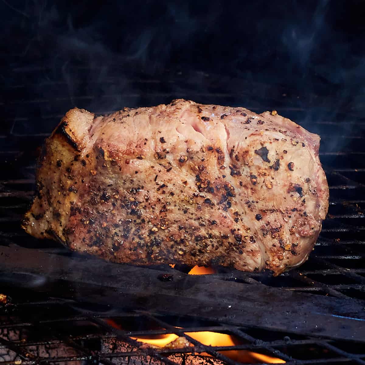 pork butt being grilled on a charcoal grill