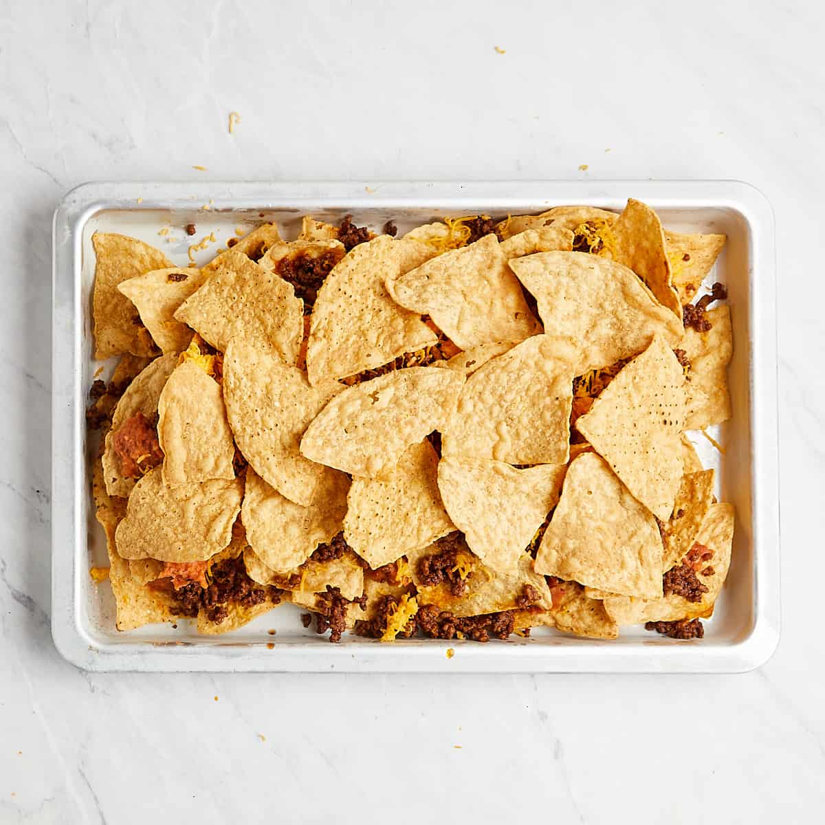 layers of tortilla chips, beans, cheese, and ground beef in a sheet pan