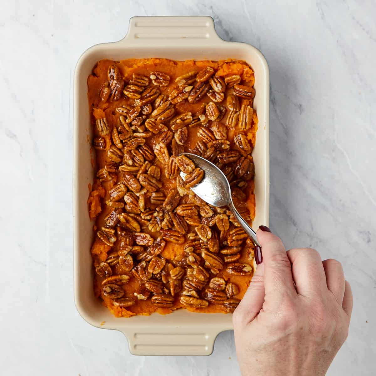 uncooked sweet potatoes in casserole with pecans being added