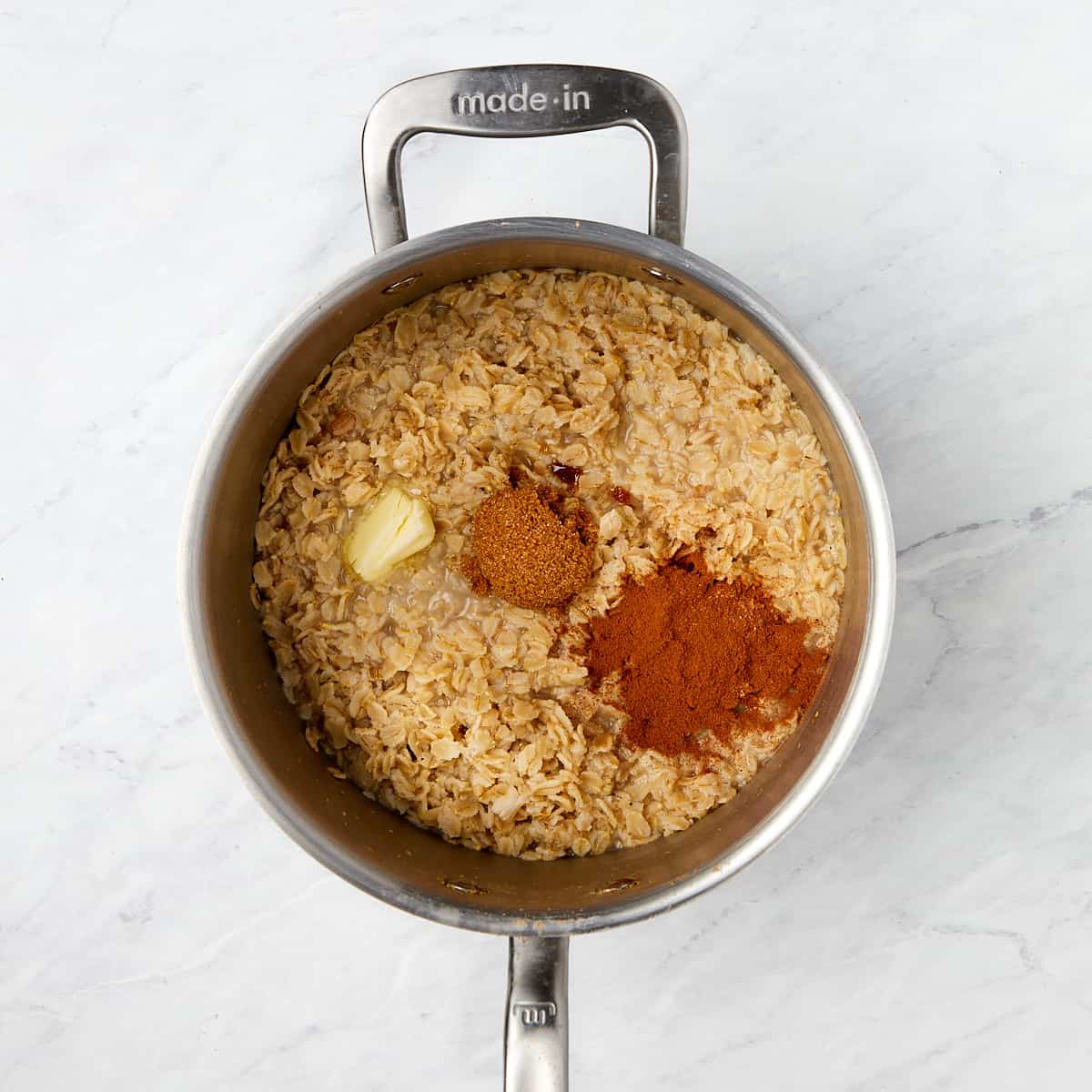 spices, brown sugar, and butter added to oatmeal cooking in saucepan