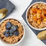 two bowls of oatmeal one topped with blueberries and one topped with cinnamon apples