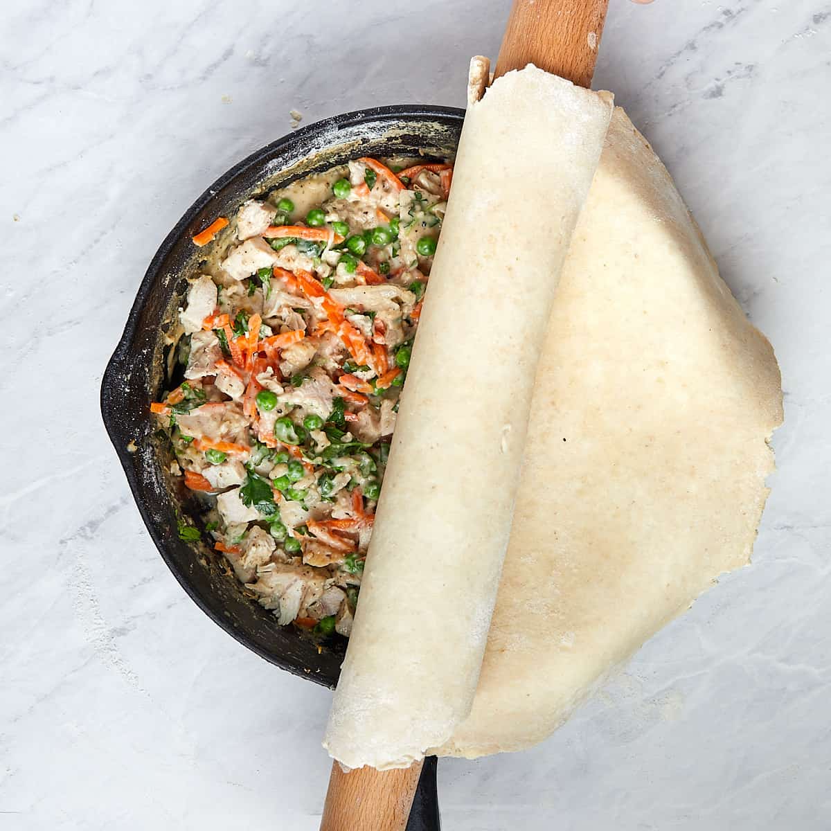 puff pastry being laid on raw pot pie in a cast iron
