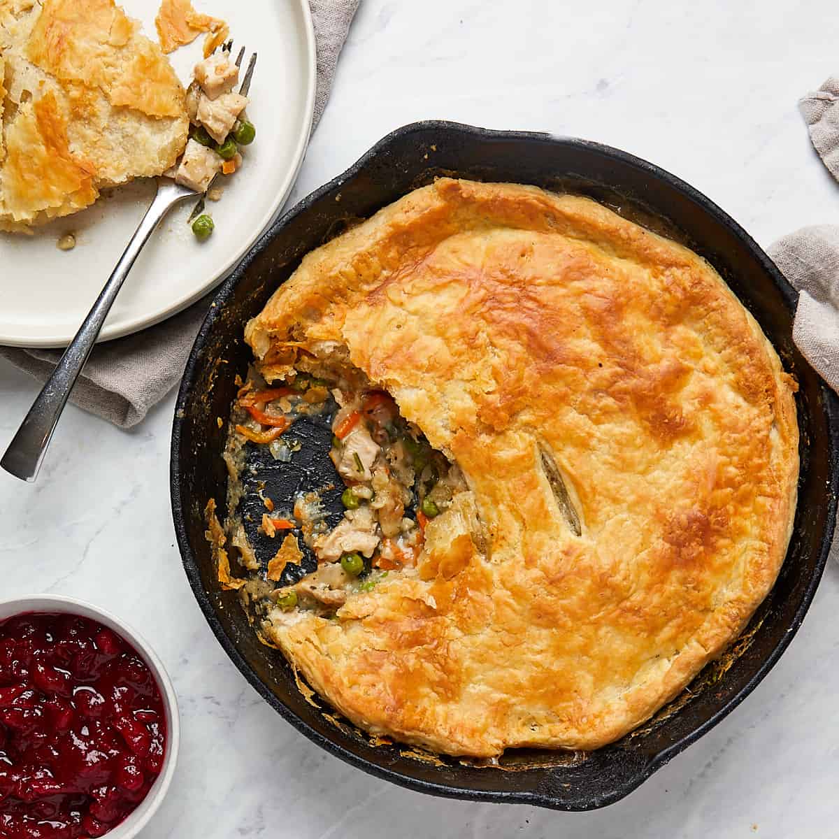 pot pie in cast iron pan with portion on a white plate and side of cranberry sauce