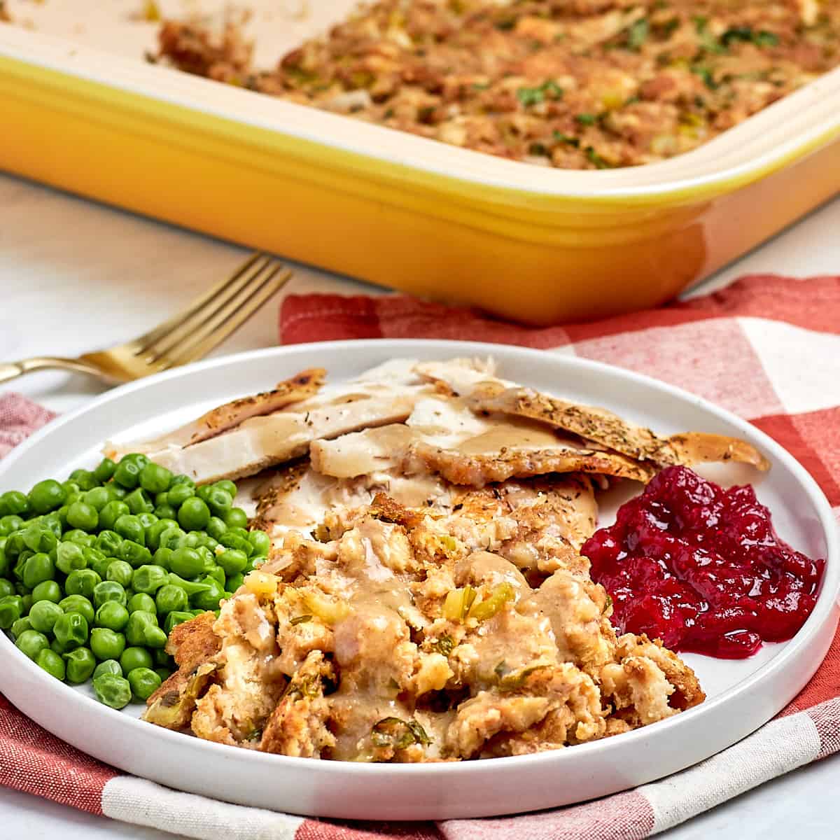 dressing with gravy on a plate with turkey, peas, and cranberry sauce