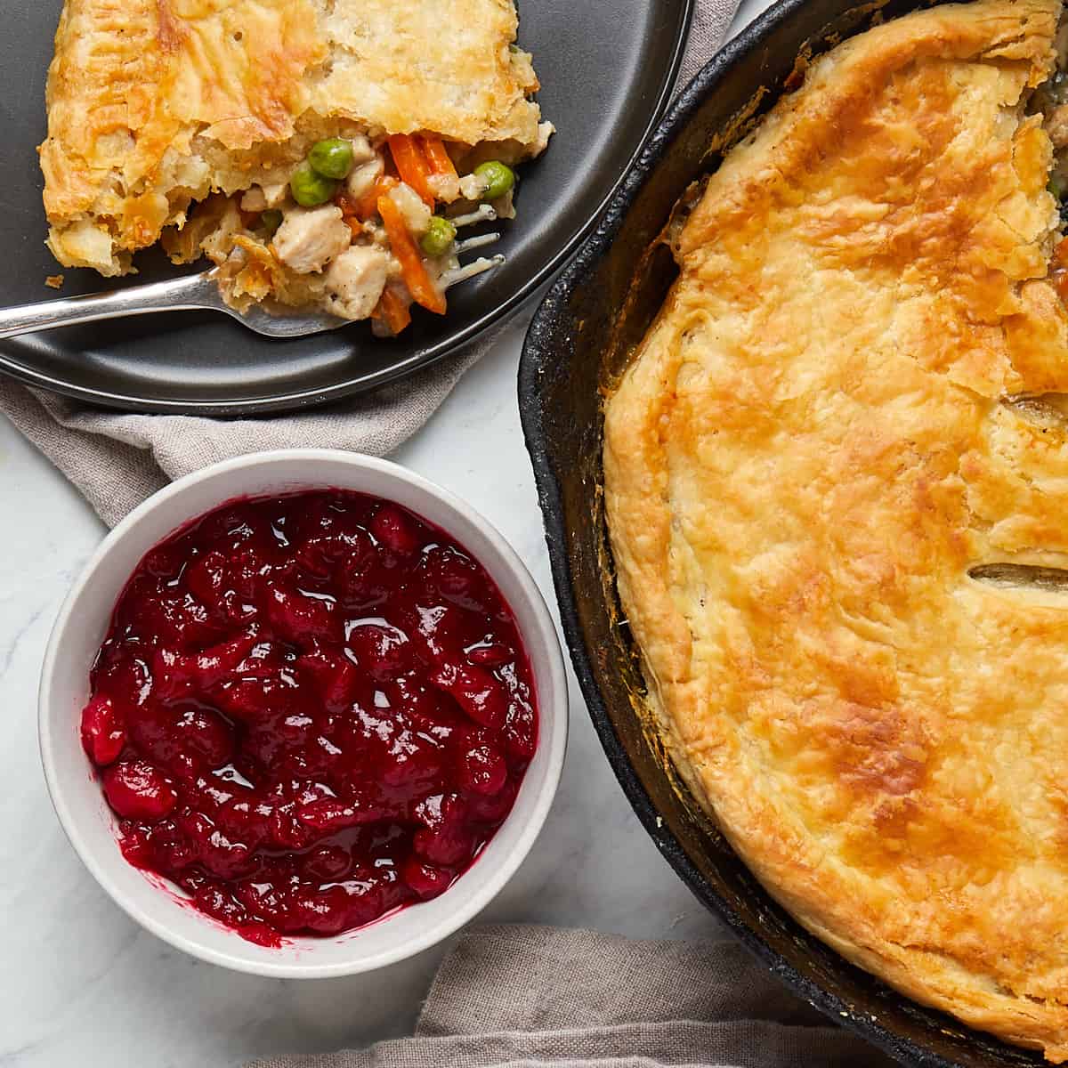 cranberry sauce in bowl served with turkey pot pie in a cast iron skillet