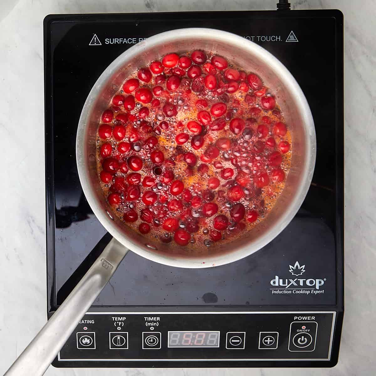 cranberries boiling with sugar, orange juice and water in a saucepan