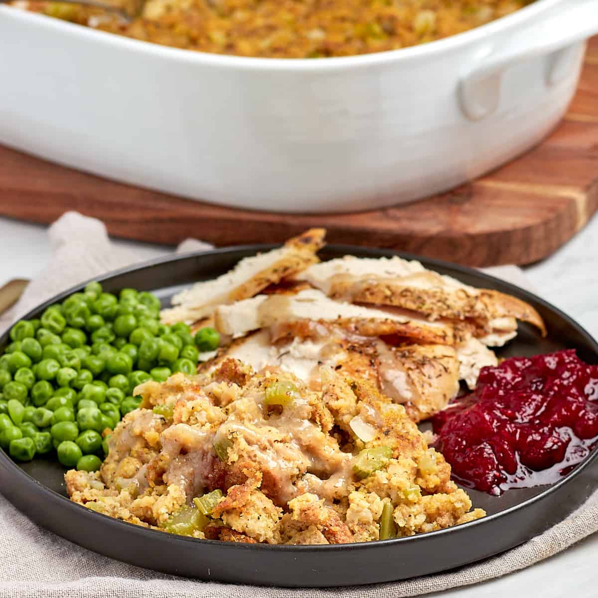 dressing on a black plate with turkey, cranberry, peas, and turkey