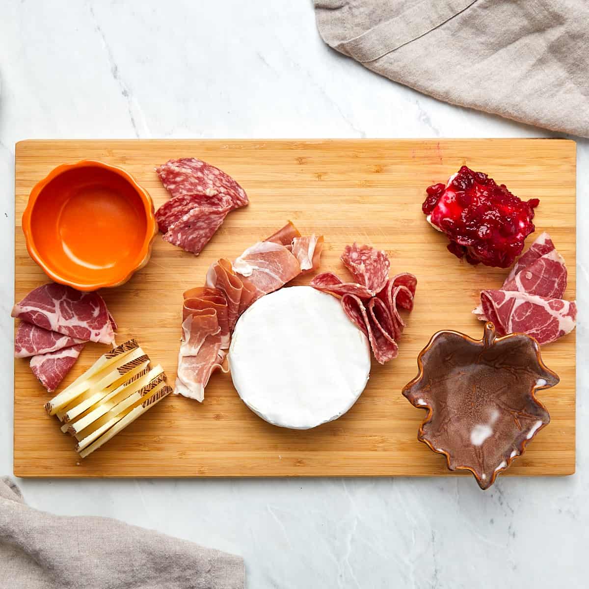 charcuterie board being assembled with cheese and meat on wood board