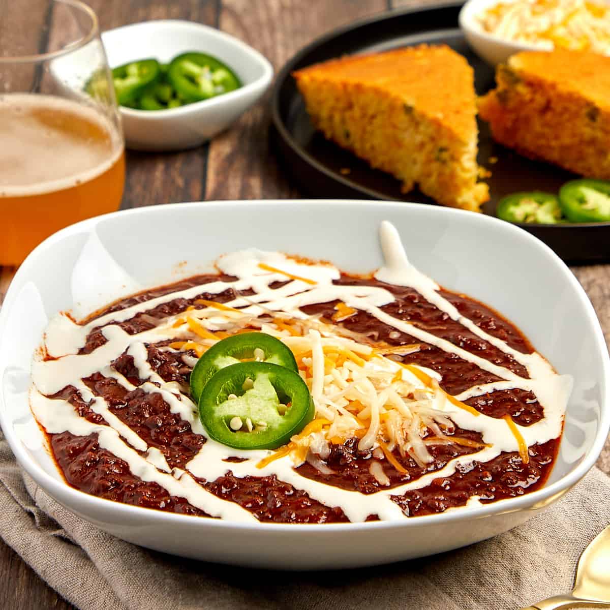 chili in a white bowl topped with crema, cheese, and jalapenos