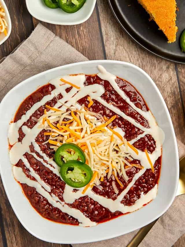 chili in a white bowl topped with crema, cheese, and jalapenos