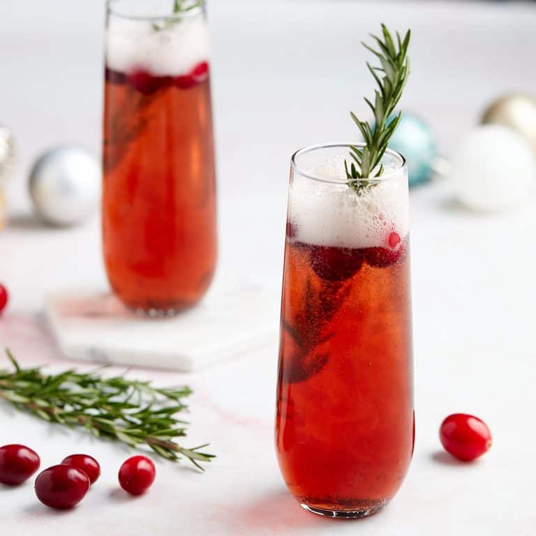manhattan spritz in a stemless champagne flute garnished with cranberries and a sprig of rosemary