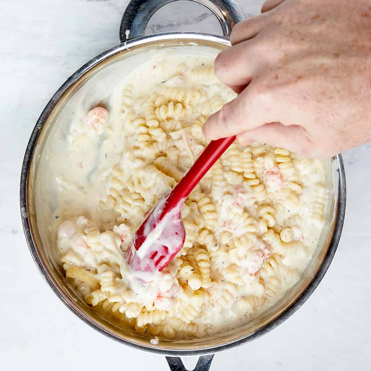 pasta being stirred into a skillet with cheese sauce with lobster