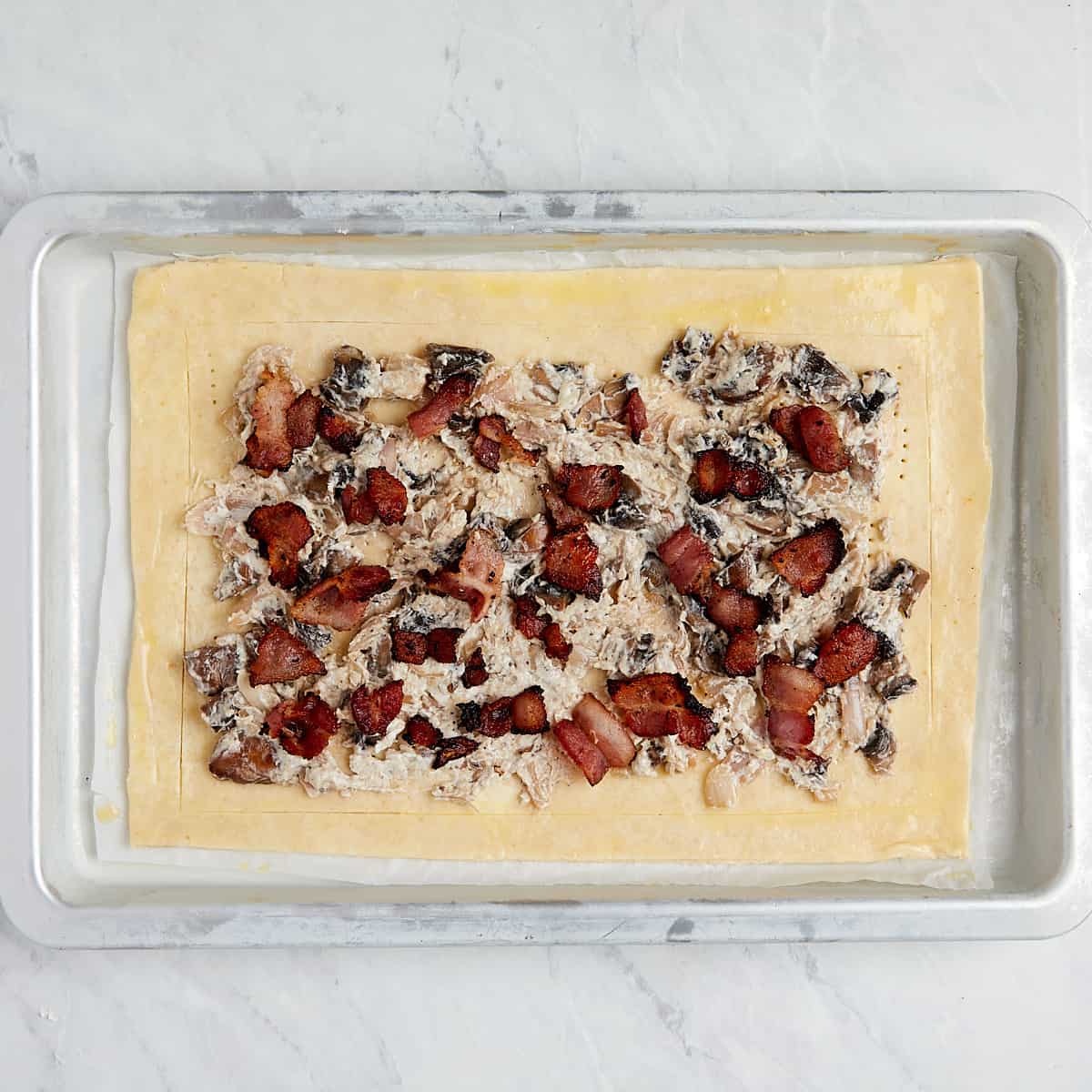 uncooked puff pastry on a cookie sheet that was topped with mushroom cheese mixture and bacon